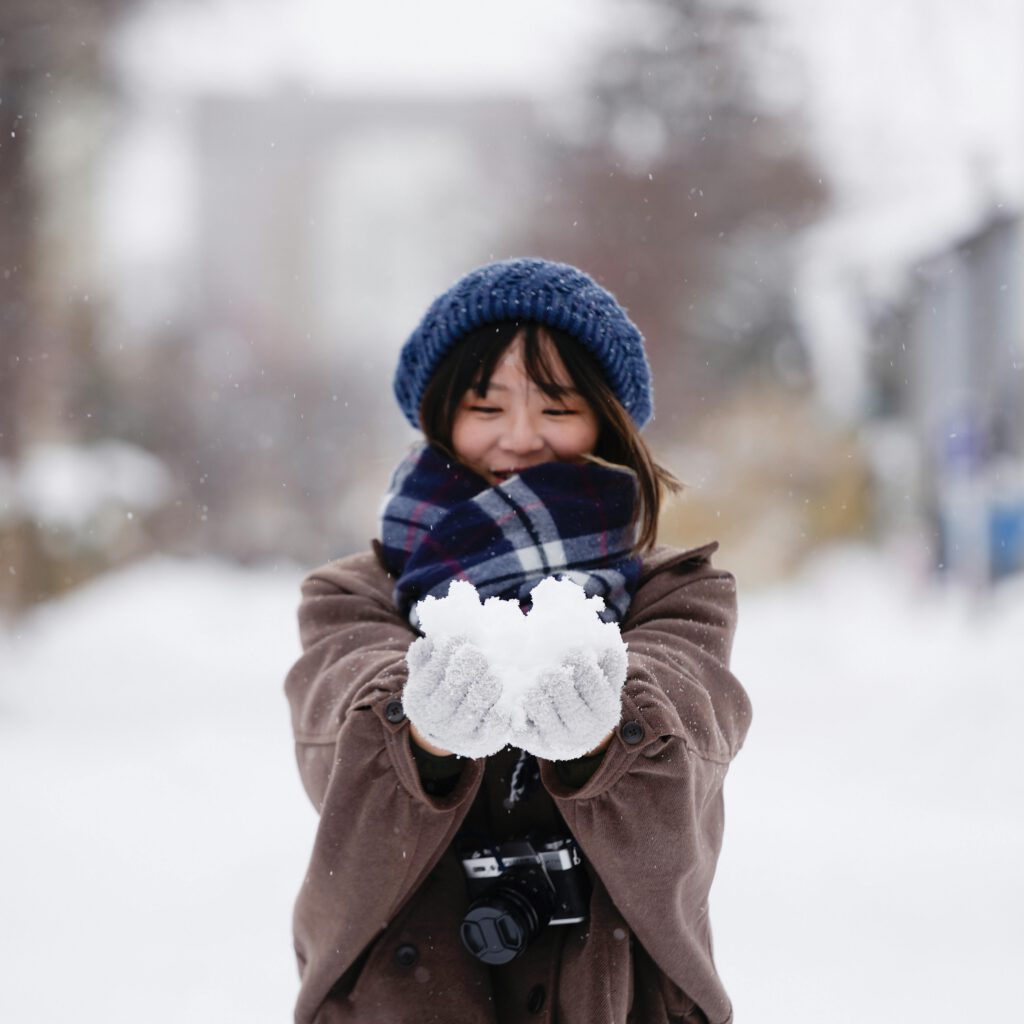 A cheerful woman holding snow, enjoying a snowy winter day outdoors.